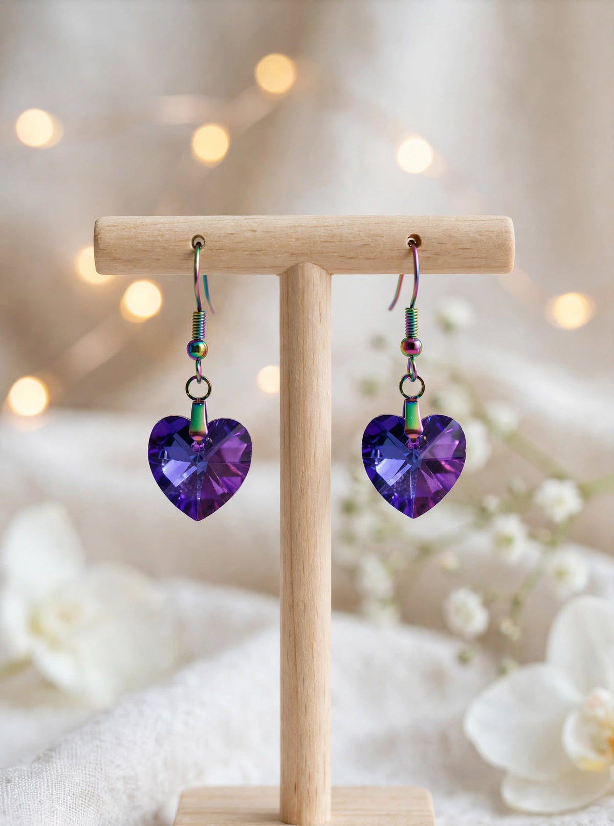 Handmade purple faceted crystal heart dangle earrings on ion-plated hooks displayed on a wooden earring stand
