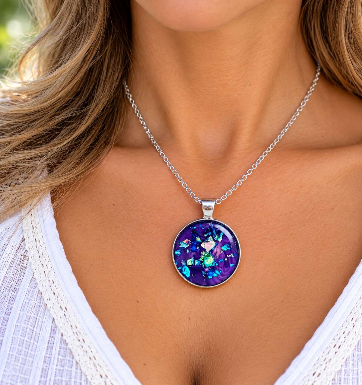 A close-up of a woman wearing a silver chain necklace with a round bezel pendant featuring a vibrant, iridescent purple and blue opal-like pattern.