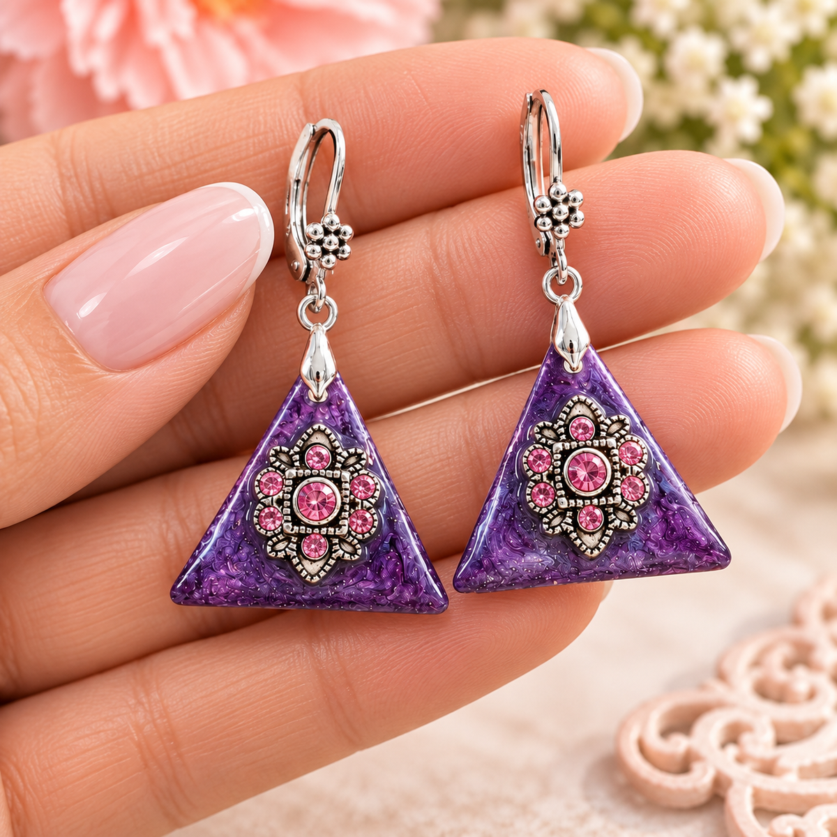 Hand holding purple rhinestone triangle earrings with pink crystal flowers