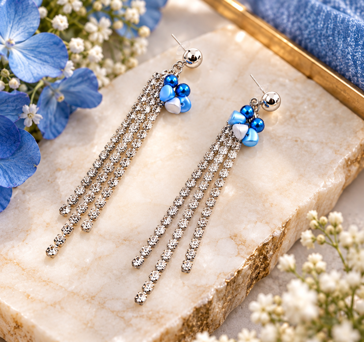 Rhinestone beaded earrings with blue beads styled on marble with blue flowers