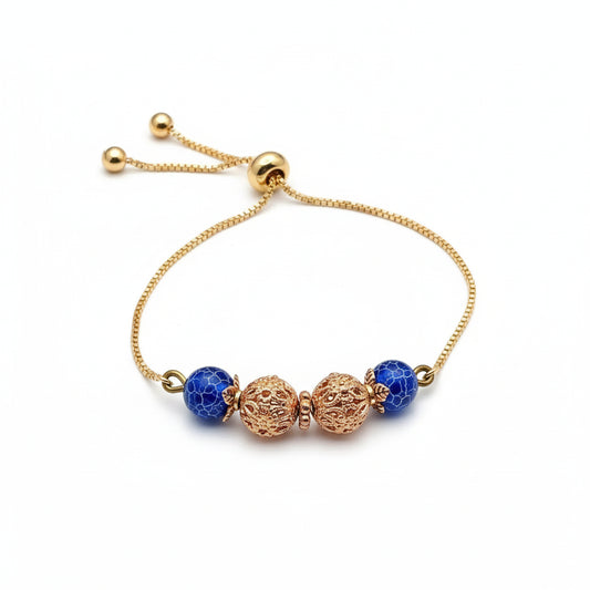 Gold bracelet with blue beads on a purple surface with a white rose.