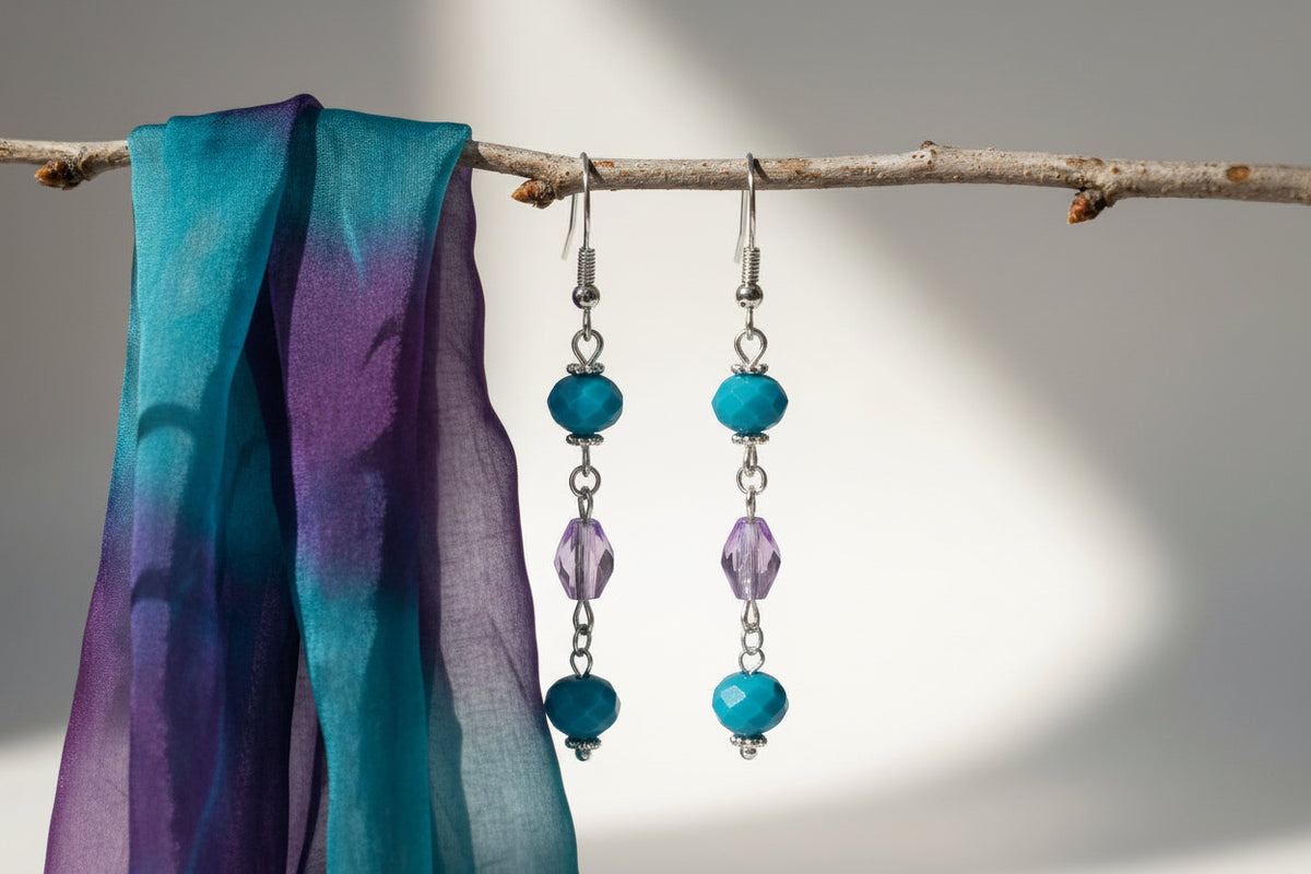 Turquoise and purple beaded earrings hanging from a branch against a neutral background