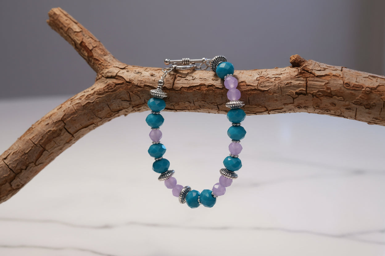 Beaded bracelet with blue and purple beads on a marble surface with a gold stand and dried flowers.