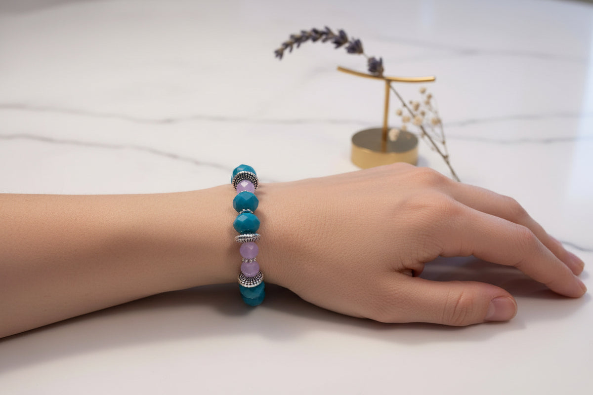 Beaded bracelet with blue and purple beads on a marble surface with a gold stand and dried flowers.
