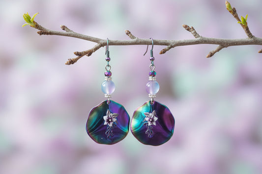 Pair of colorful earrings with floral design hanging on a branch against a gray background