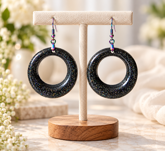 Black resin hoop earrings with glitter on a display stand