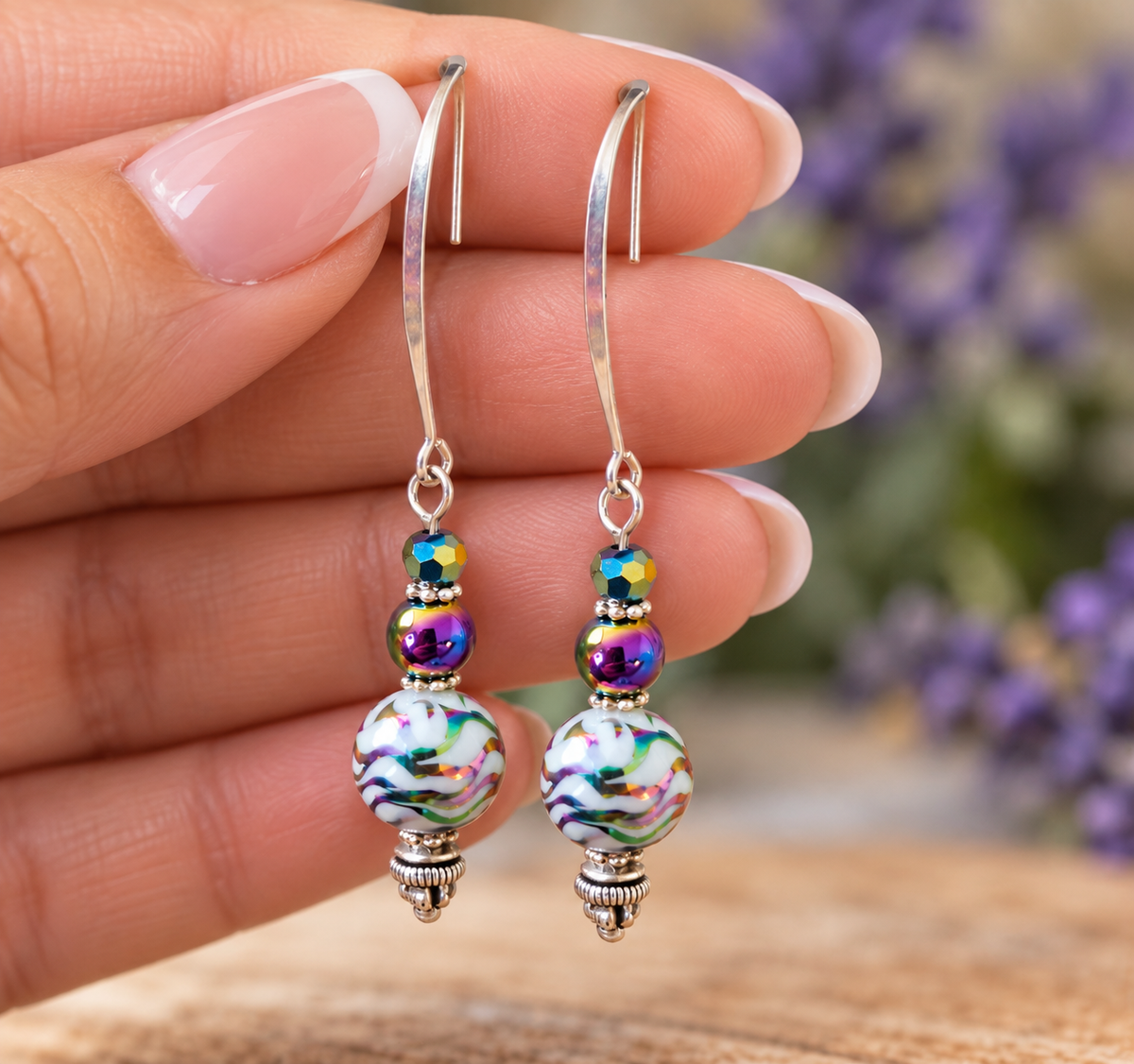 Close-up of hand holding handmade rainbow hematite dangle earrings with silver kidney hooks