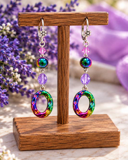 Rainbow ion plating dangle earrings with lavender crystals on a display stand