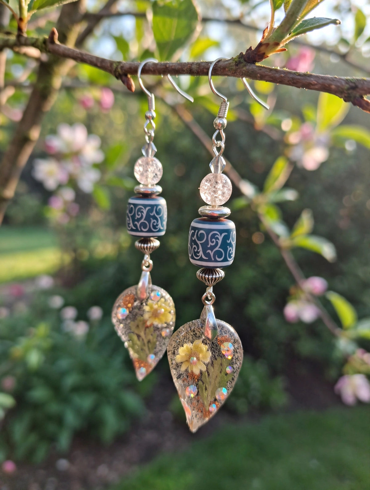 Pair of dried flower resin leaf dangle earrings with teal boho glass beads and clear crystal beads on a branch