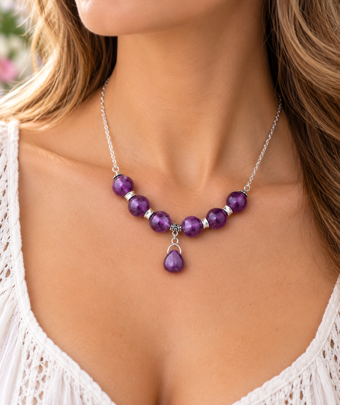 A close-up of a woman wearing a silver necklace with purple gemstone beads and a teardrop pendant.
