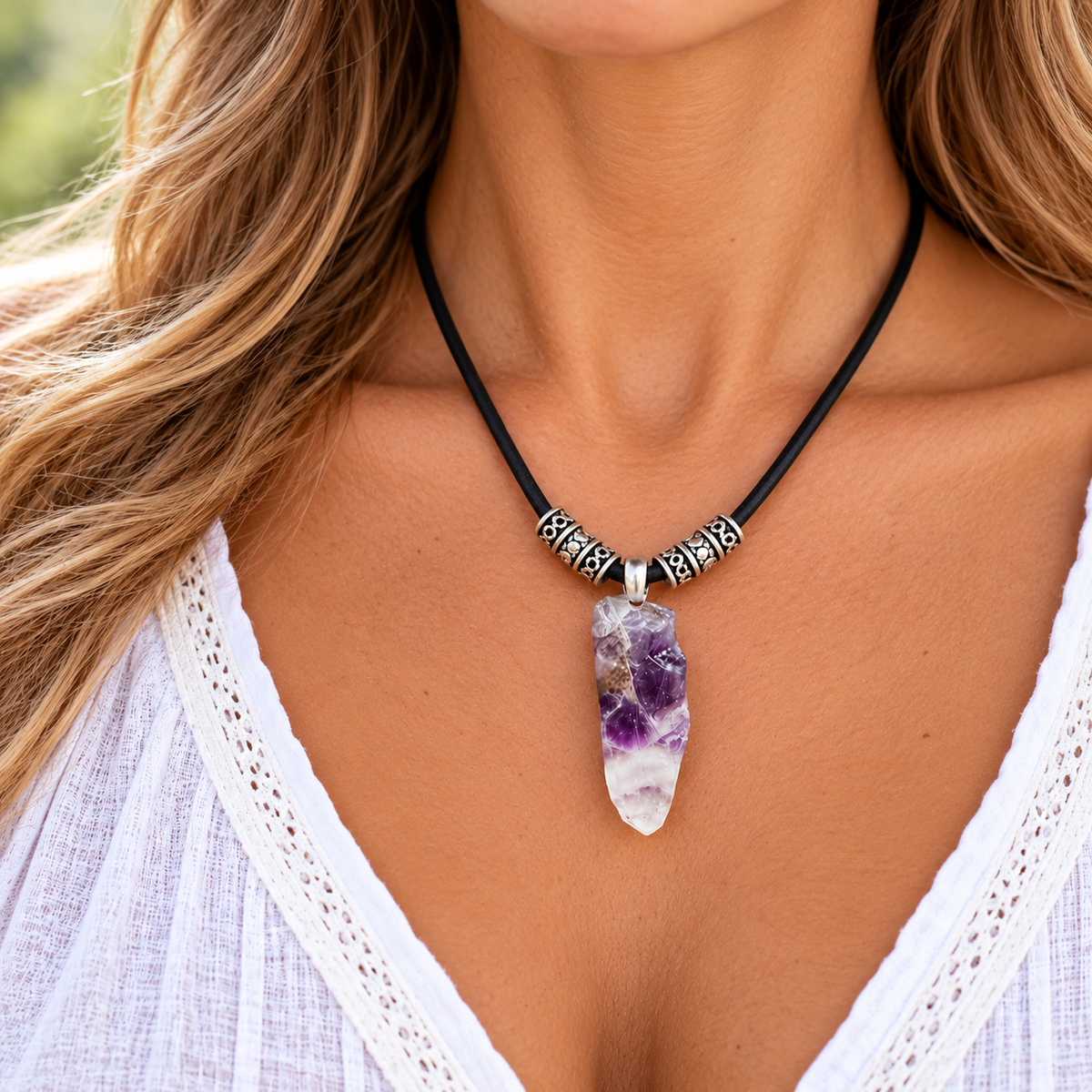 A close-up of a woman wearing a black cord necklace with silver-toned geometric spacer beads and a natural amethyst crystal pendant.