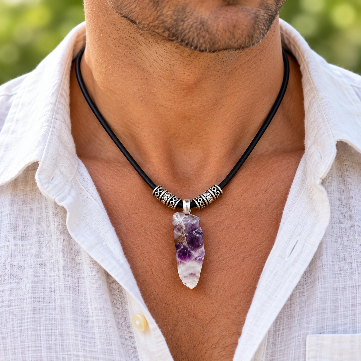 A man wearing a black cord necklace with silver spacer beads and a raw amethyst crystal pendant, styled with a white linen shirt.