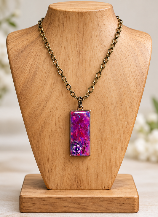 A rectangular pendant necklace with a vibrant purple and magenta marbled design, displayed on a light wood mannequin bust with an antique bronze chain.