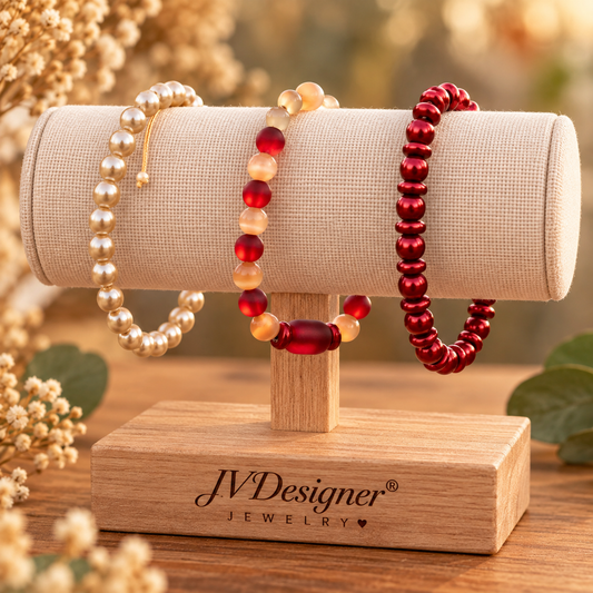 Three beaded and pearl bracelets displayed on a cylindrical fabric jewelry stand mounted on a wooden base. The stand is engraved with the brand name 'JVDesigner Jewelry'.