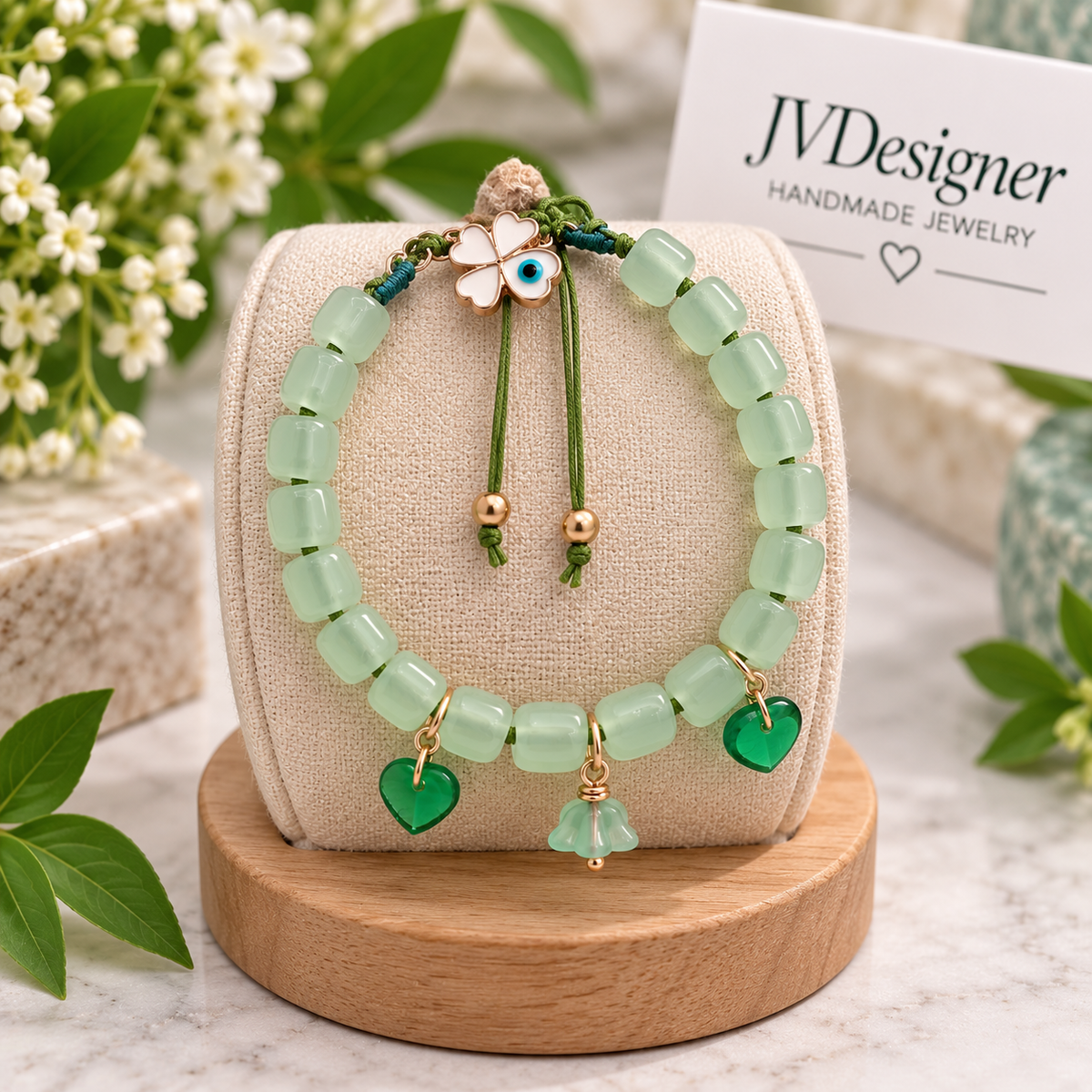 A beaded bracelet and matching earrings displayed on a beige fabric stand on a wooden base. The jewelry features light green translucent beads, green heart charms, a green evil eye pendant, and gold-tone accents.