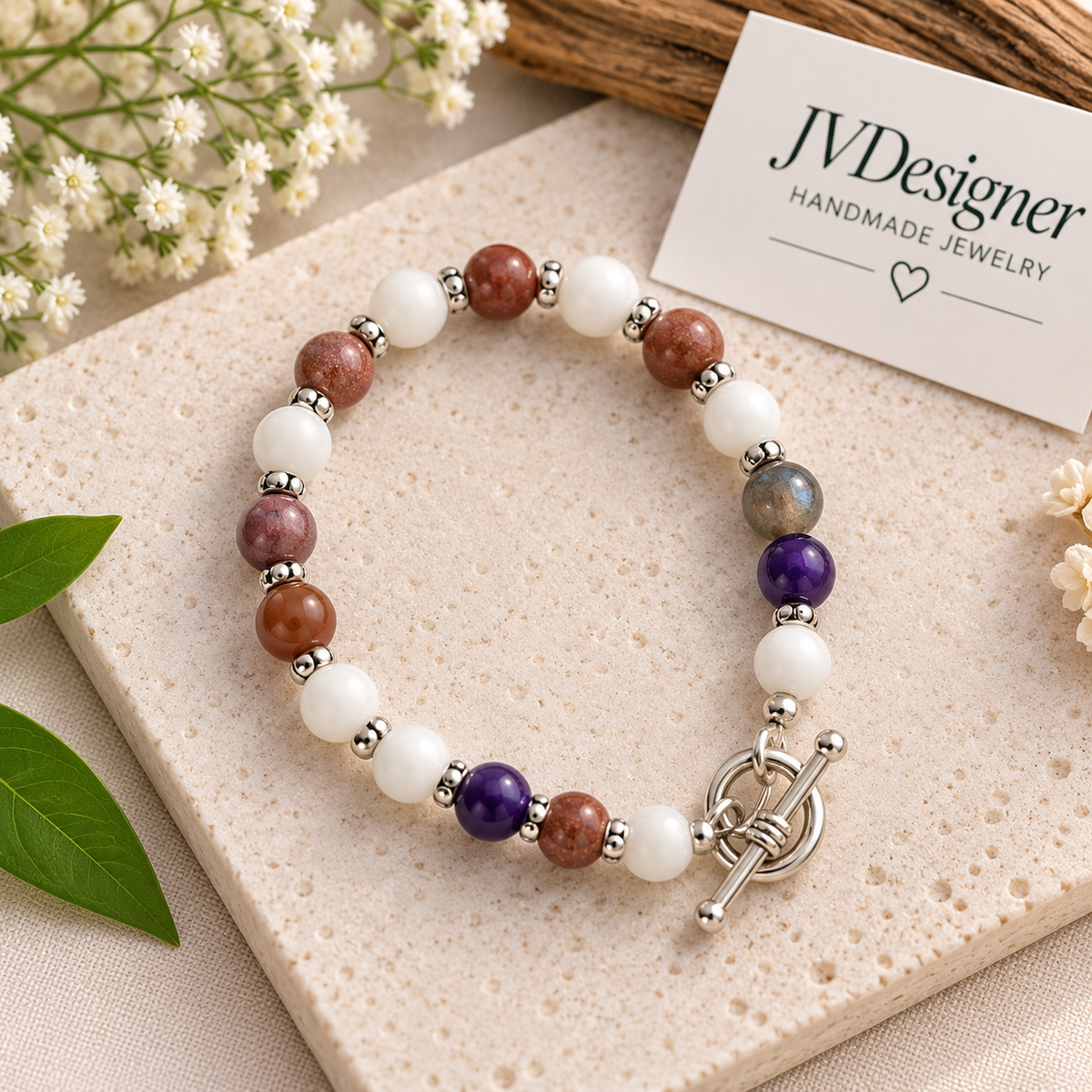 “Handmade gemstone bracelet with white, brown, purple and gray beads and silver accents on a round stone display.”