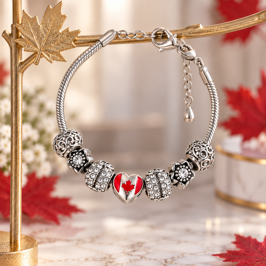 A silver-toned snake-style charm bracelet displayed on a gold branch stand. The bracelet features five decorative beads, including a central heart charm with a red maple leaf on a white background, and clear rhinestone accents.