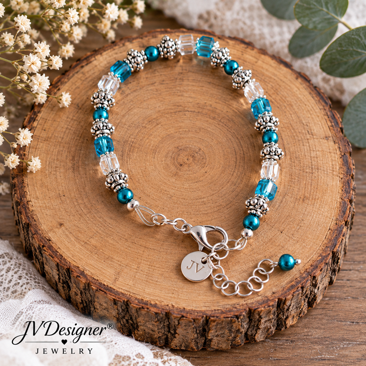 A beaded bracelet with turquoise blue beads, clear faceted beads, and silver-toned spacer beads, displayed on a round wood slice. The bracelet has a lobster clasp, extender chain, and a round initial charm engraved with 'M'.