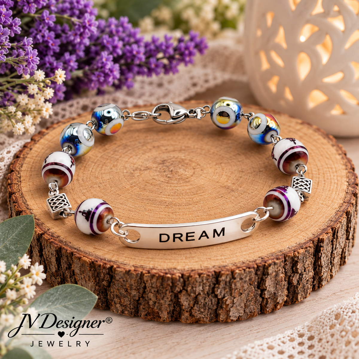 A charm bracelet displayed on a rustic wood slice. The bracelet features colorful glass evil eye beads, striped white beads, silver spacer beads, and a central silver bar engraved with the word 'DREAM'.