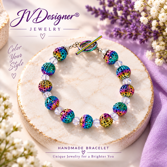A handmade beaded bracelet with iridescent multicolor beads and a matching clasp, displayed on a round stone slab with decorative flowers and purple fabric. The brand name 'JVDesigner Jewelry' is visible in the top left.