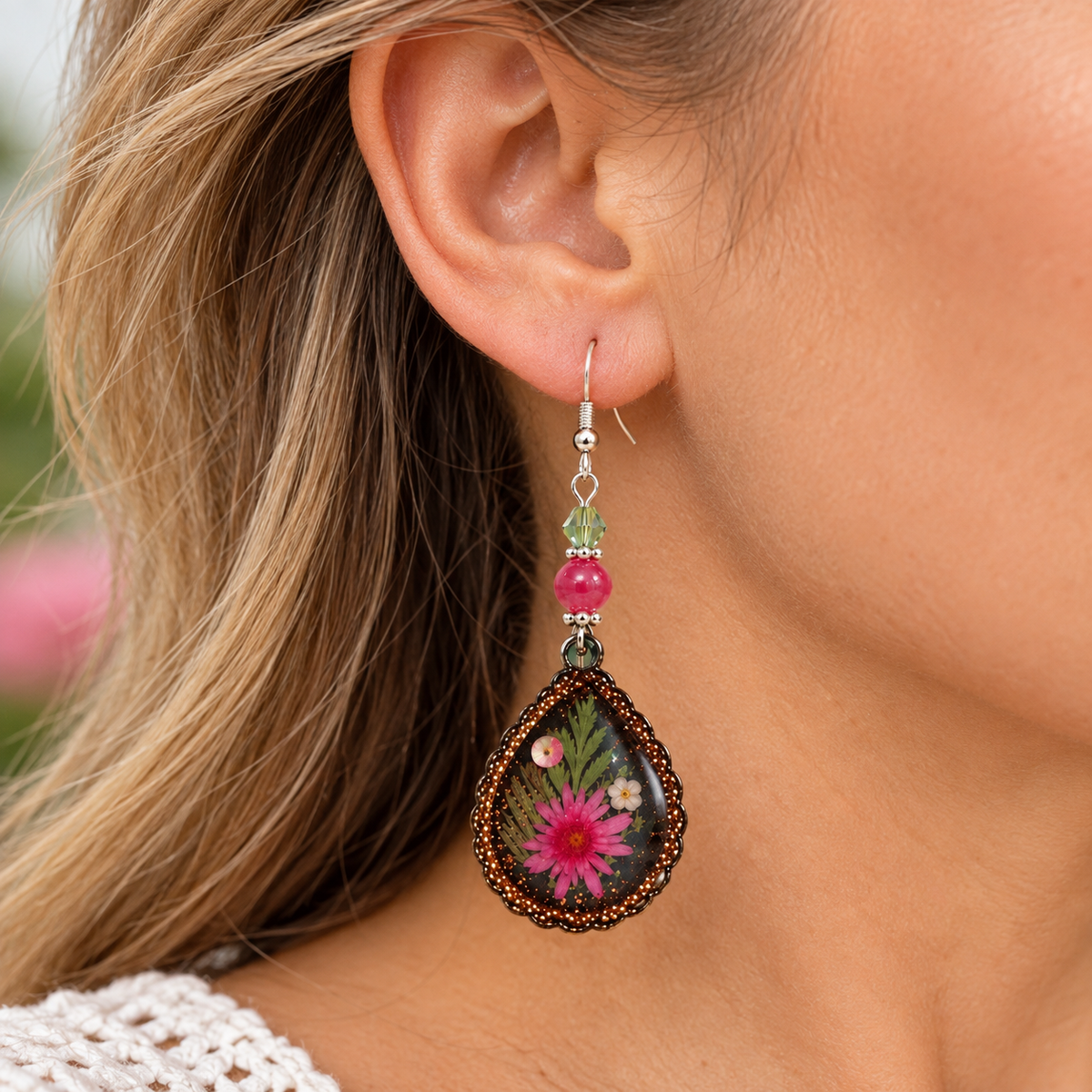 Model wearing pink daisy resin teardrop dangle earrings with bronze beaded edge, silver-tone fish hooks, and pink and light green bead accents