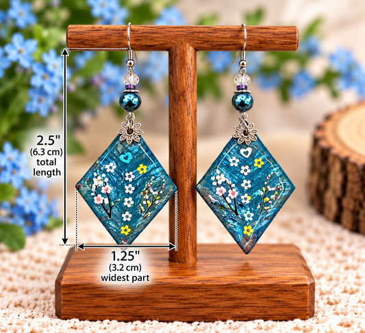 A pair of dangling earrings displayed on a wooden stand, with overlaid dimension lines showing a total length of 2.5 inches (6.