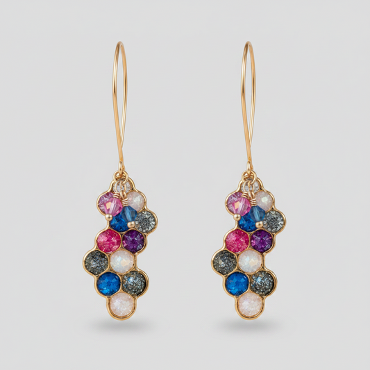 A split image showing a pair of gold hoop drop earrings with a cluster of colorful gemstones. The left side shows the earrings worn on a person's ear, and the right side shows a close-up of the earrings hanging from a tree branch with a blurred garden background.