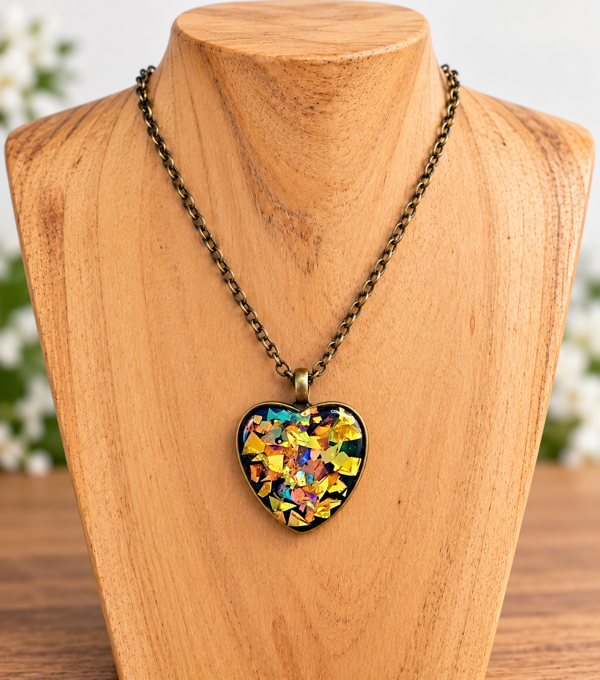 A heart-shaped pendant necklace with a colorful mosaic design, hanging on an antique bronze chain from a wooden display bust.