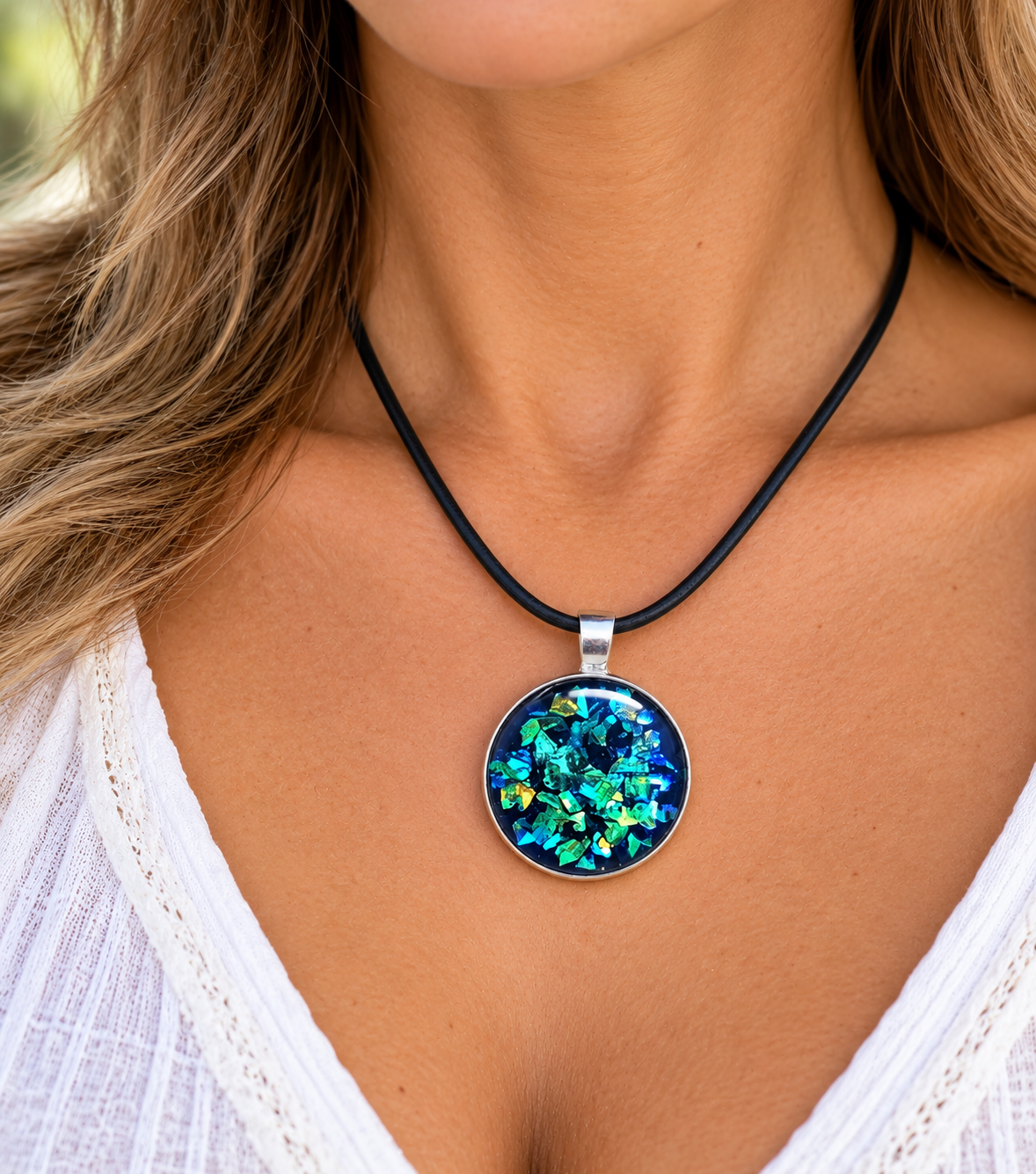 A close-up of a woman wearing a round pendant necklace with a black cord and a silver-toned bezel. The pendant contains a colorful, iridescent blue and green opal-like pattern.