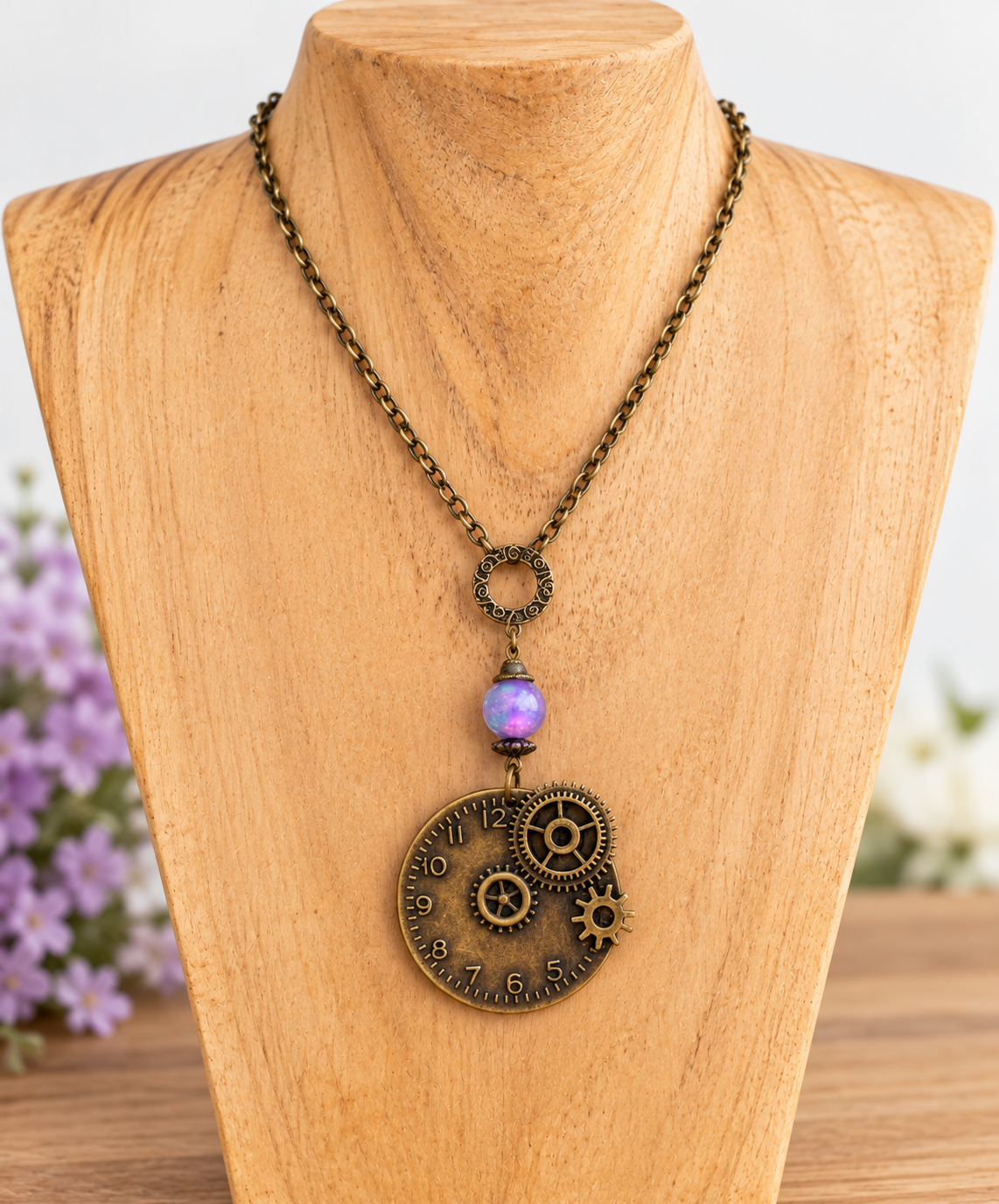 Steampunk-style necklace displayed on a wooden bust, featuring an antique bronze chain, a purple iridescent bead, and a circular gear pendant with clock-face detailing.