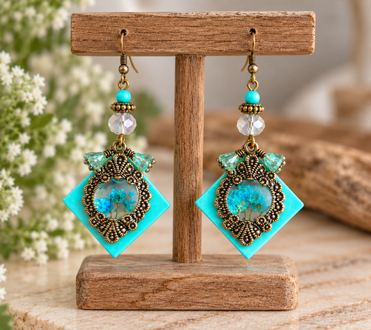 Antique bronze square resin earrings with blue floral cabochons on a display stand