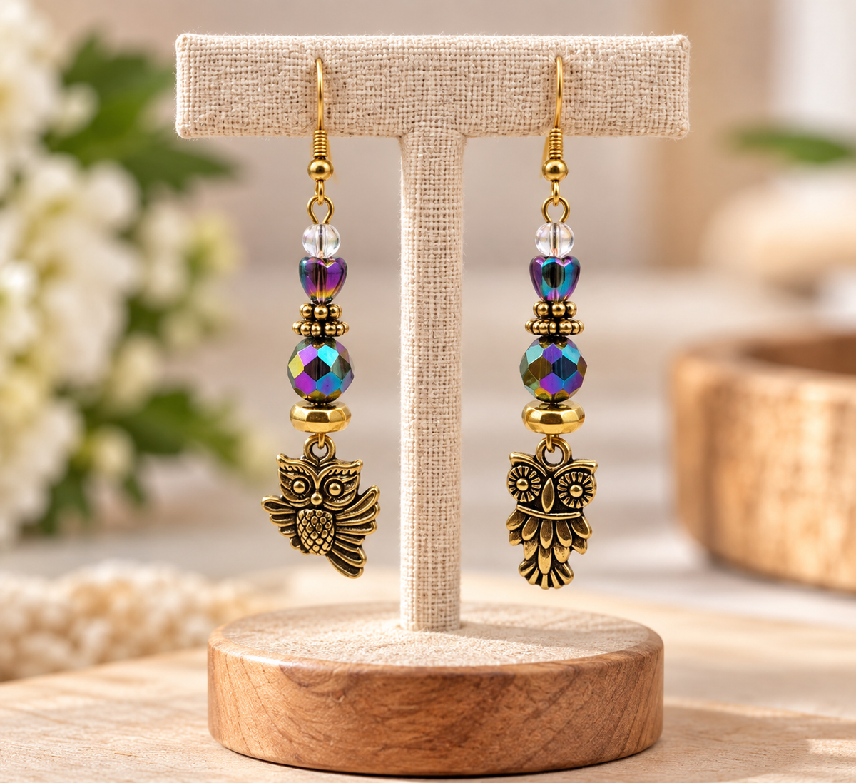 Gold owl dangle earrings with iridescent crystal beads on a display stand