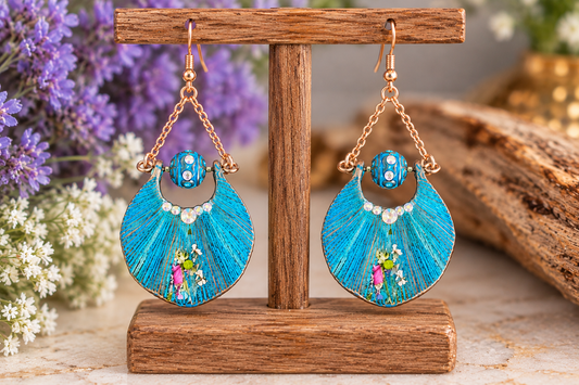 Blue patina resin crescent dangle earrings with dried flowers on a display stand