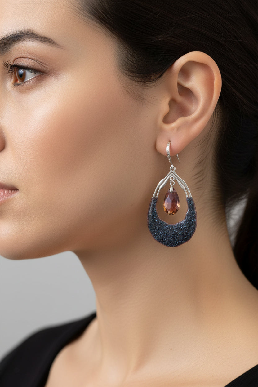 Teardrop-shaped earrings with dark blue and red gemstones hanging on a branch.