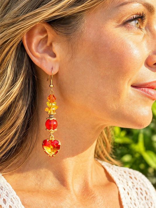 Close-up of a model wearing a gold dangle earring with orange crystal beads and a red-orange heart pendant