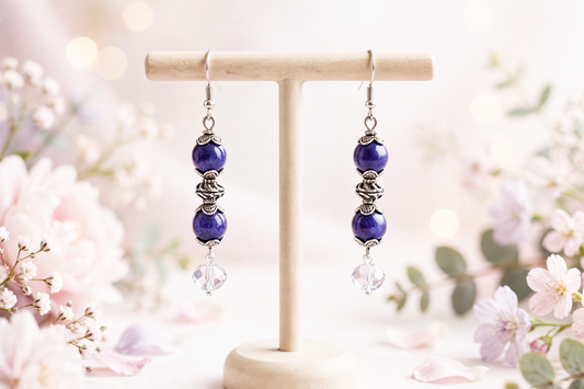 Handmade purple glass bead dangle earrings with silver accents and crystal drops on a wooden stand