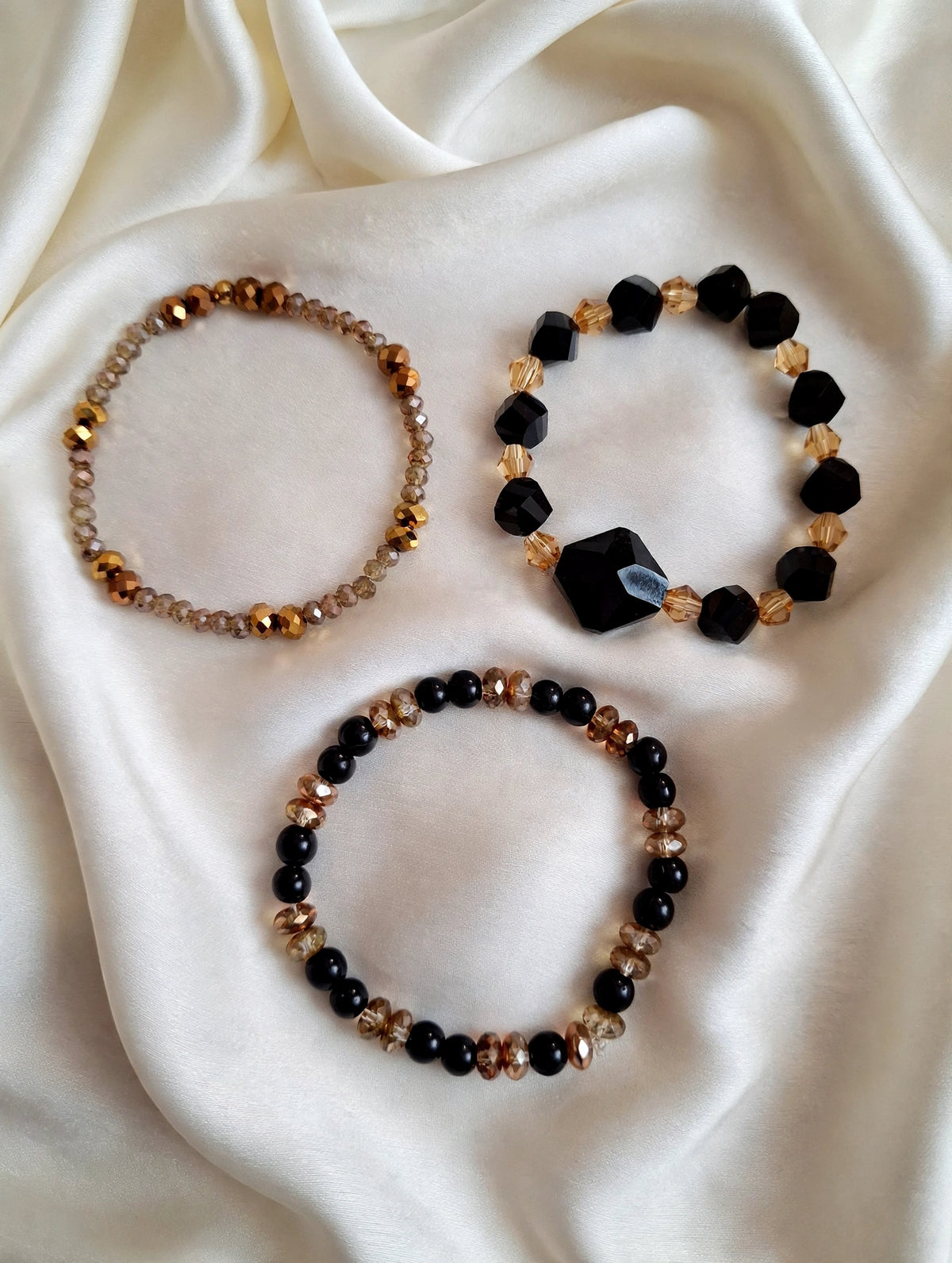 Set of 3 handmade black and gold glass bead stretch bracelets in perfect circles on ivory silk