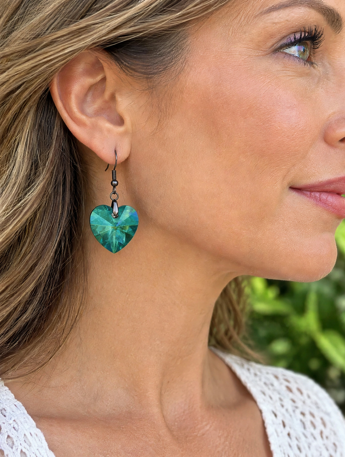 A close-up side profile of a woman wearing a dangling heart-shaped earring with a green marbled pattern and a small black bead charm.