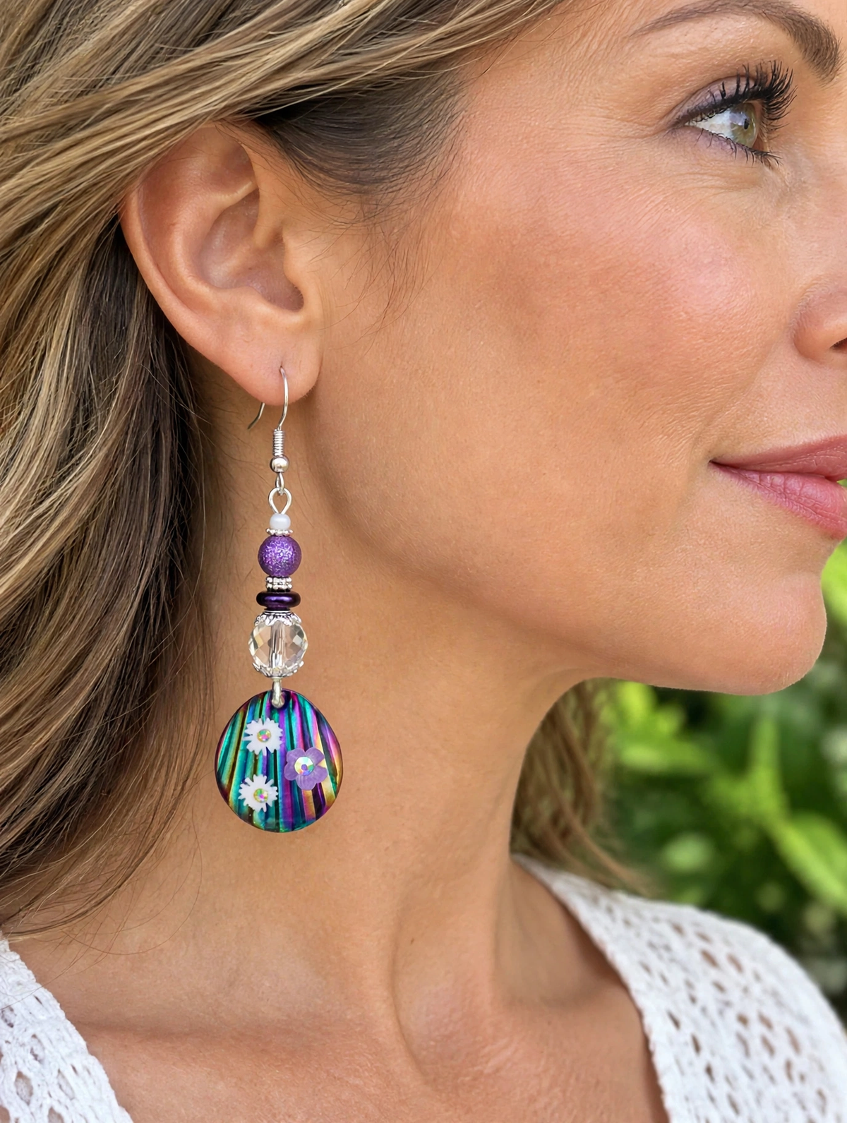 Model wearing handmade rainbow floral teardrop dangle earring with purple bead and crystal