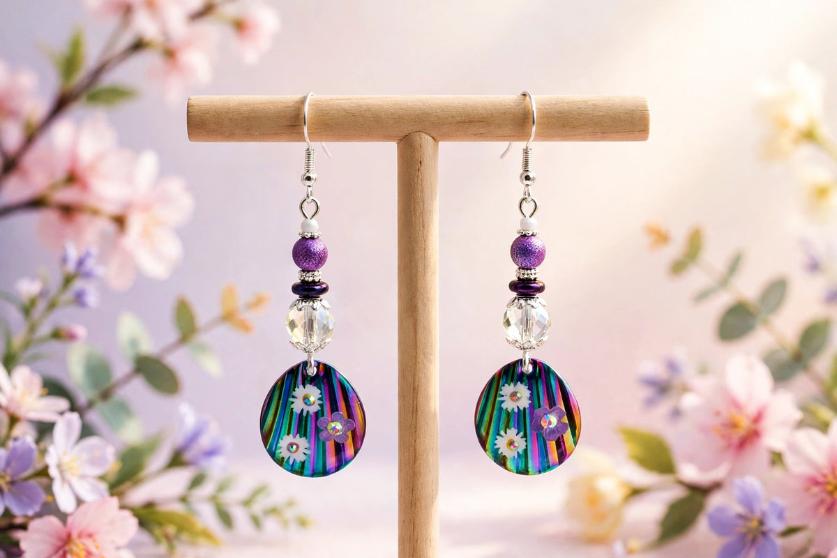 Handmade rainbow floral disc dangle earrings with purple beads on a wooden stand against blossoms