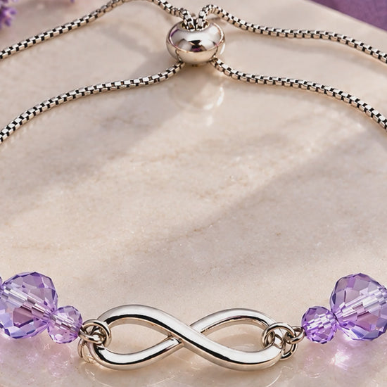 Silver infinity bracelet with lavender AB crystals, adjustable bolo closure, on marble with lavender flowers"
