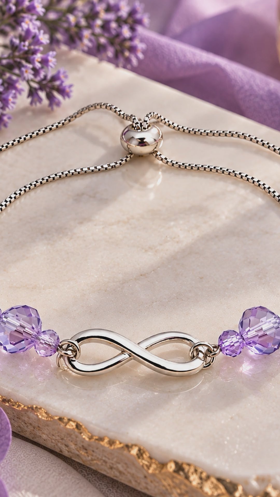 Silver infinity bracelet with lavender AB crystals, adjustable bolo closure, on marble with lavender flowers"